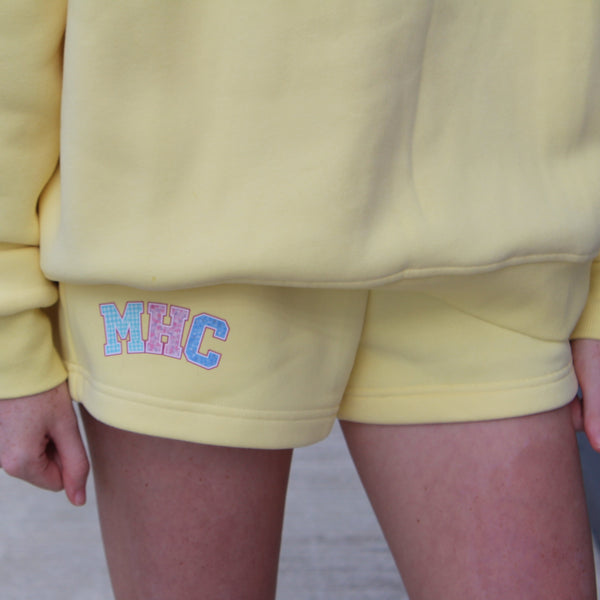Person wearing a yellow sweatshirt and shorts with colorful text on a blurred background
