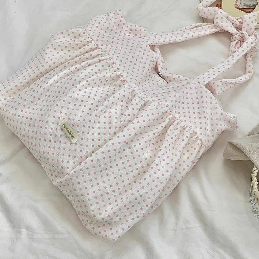 Pink polka dot bag on a light surface with books and a hat.